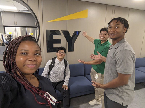 Interns point to EY sign at workplace.