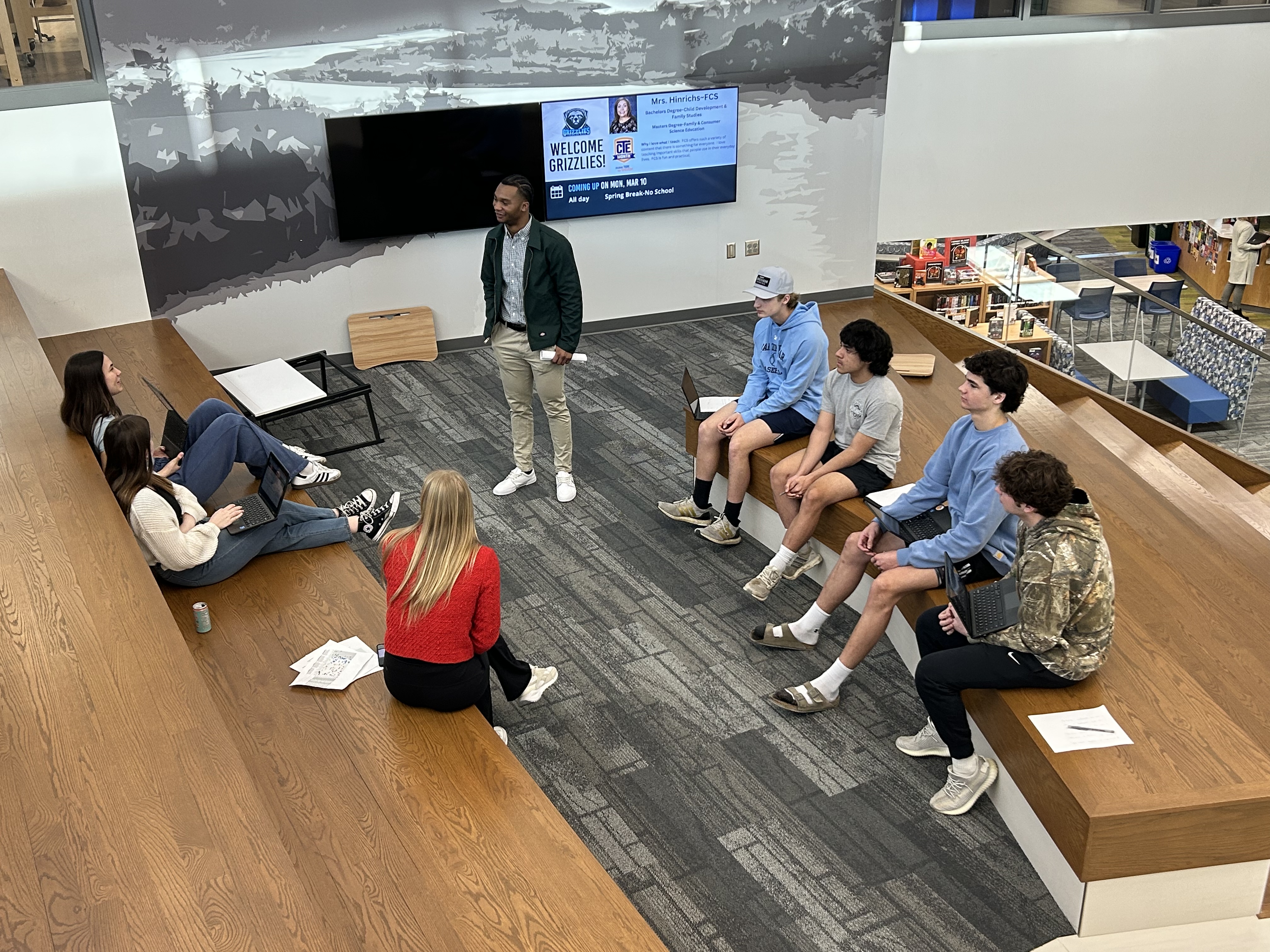 Dywan standing and talking to high school students sitting around him.