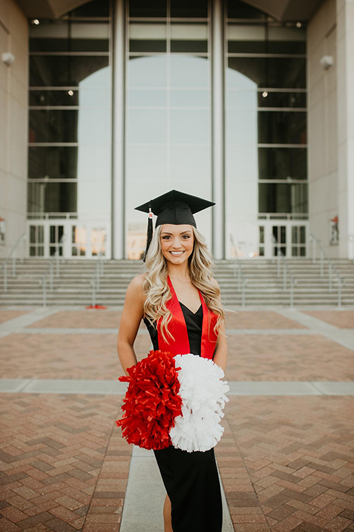 Sydney stands outside the stadium in graduation cap.