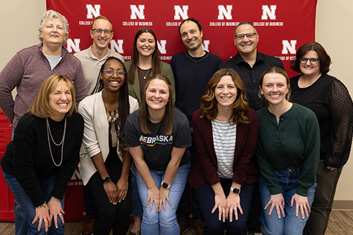 Nine of the ten College of Business staff pose in front of a branded backdrop.