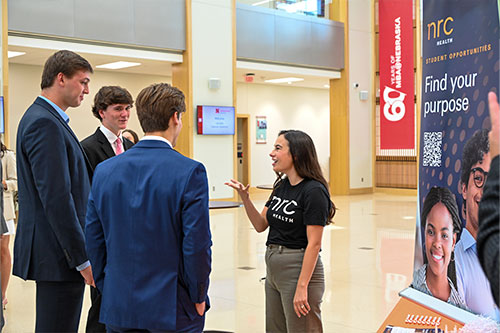 Three male students in suits talk to a female recruiter from NRC Health.